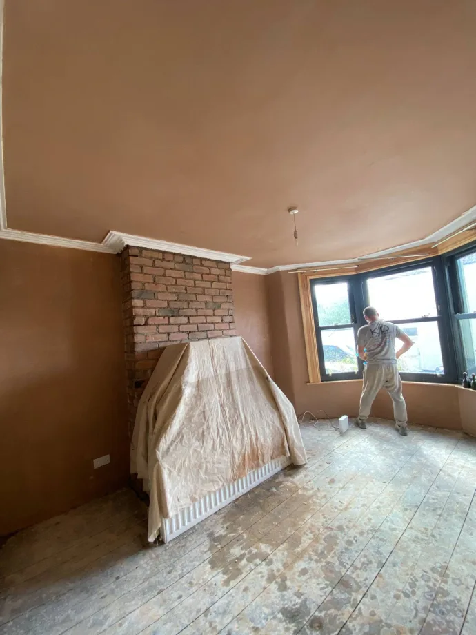 Plasterer at a bay window beside a skimmed chimney breast