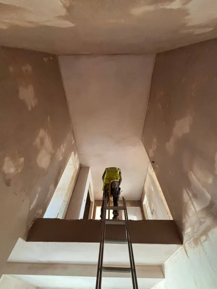 Stairwell seen from below, walls and soffit skimmed, plasterer working at the head
